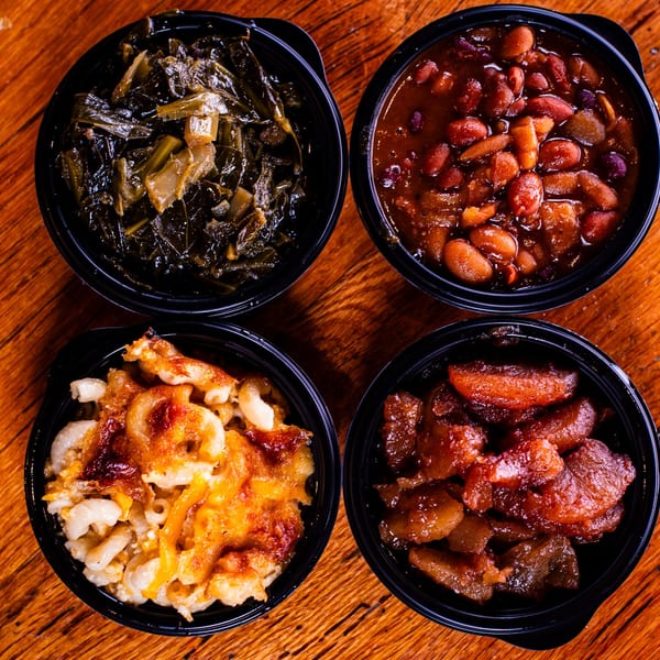 Four bowls of Southern sides: collard greens, baked beans, macaroni and cheese, and candied yams.