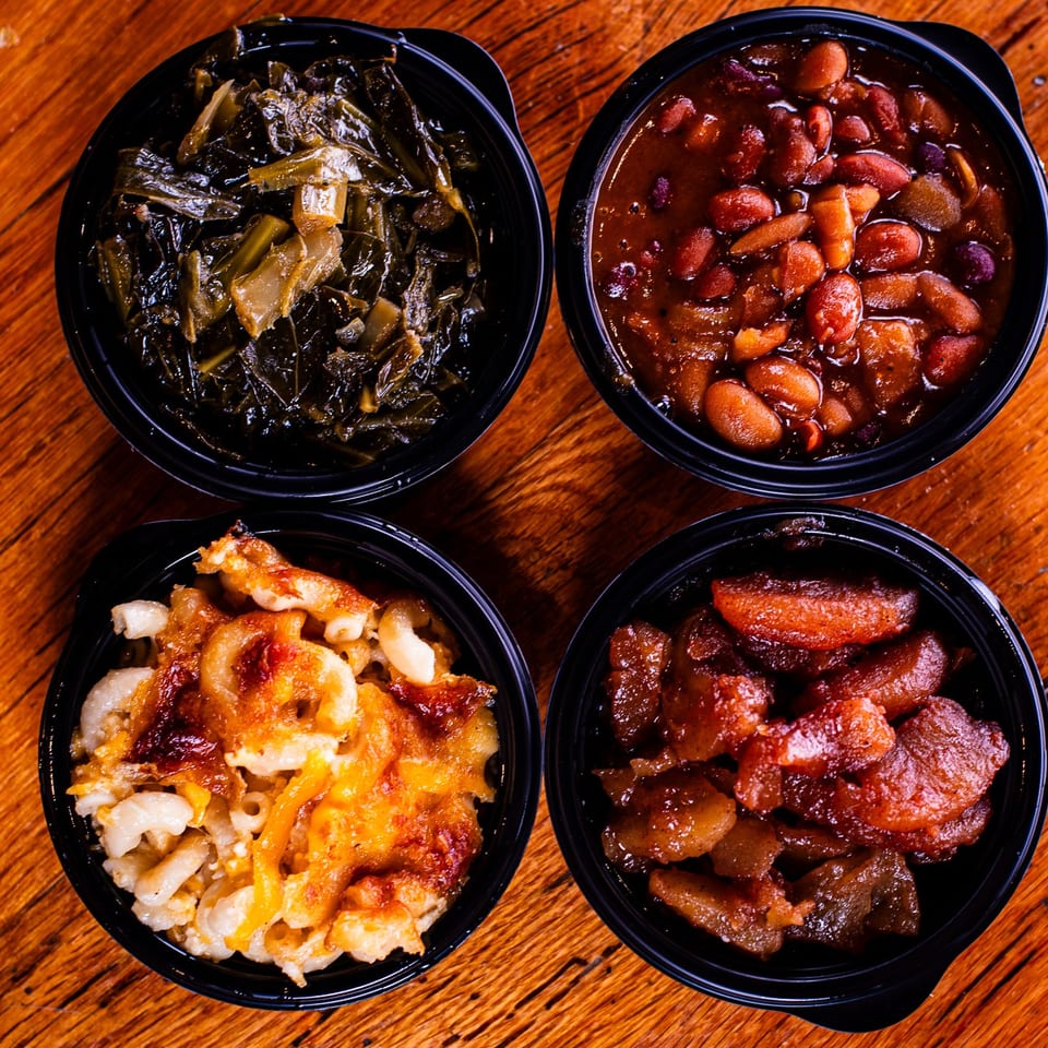 Four bowls of Southern sides: collard greens, baked beans, macaroni and cheese, and candied yams.
