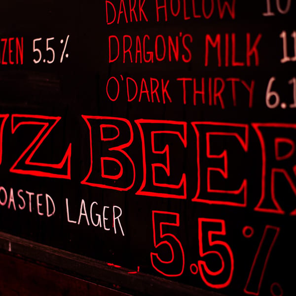 Chalkboard menu with red and white text listing beer names and alcohol percentages.