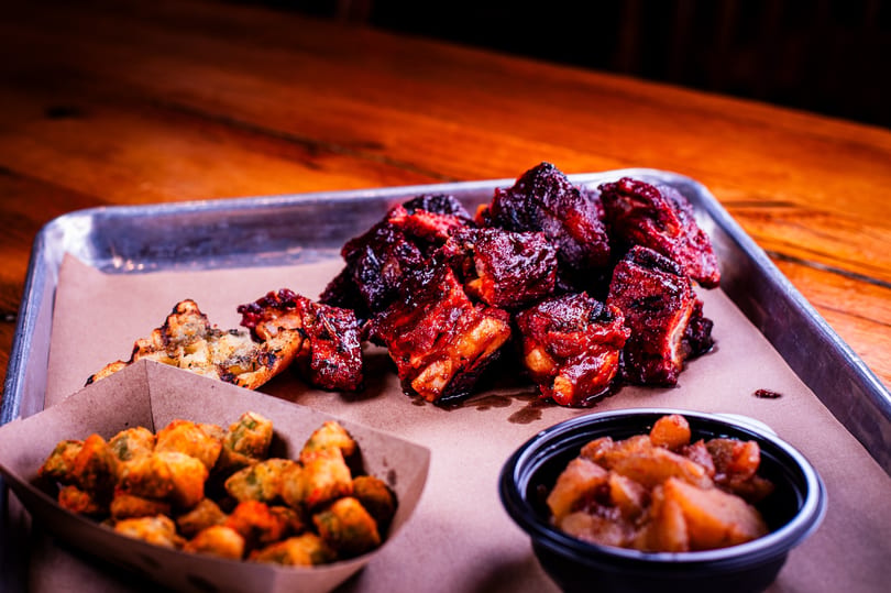 Platter of saucy BBQ ribs, fried okra, and baked apples on a metal tray.