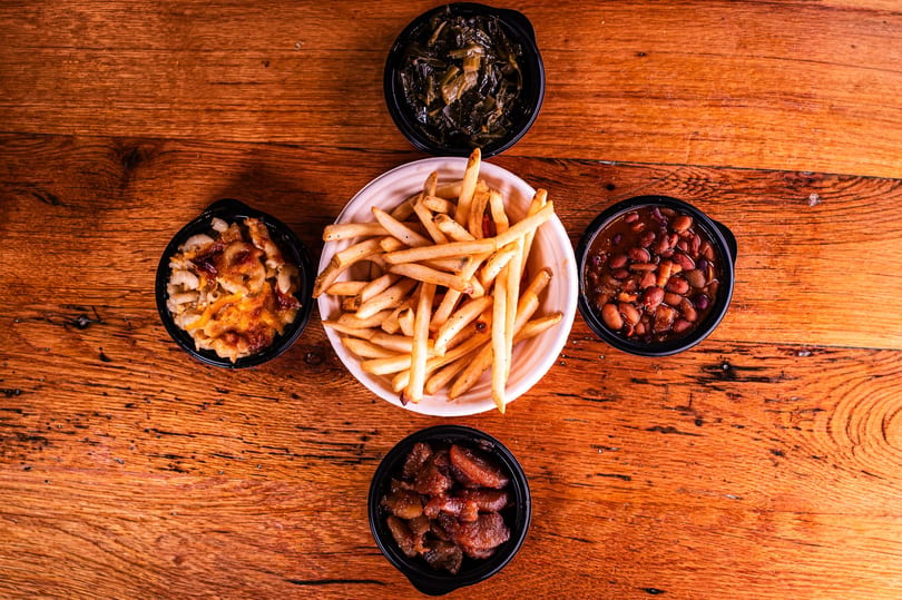 Assortment of sides including french fries, mac and cheese, collard greens, baked beans, and candied yams.